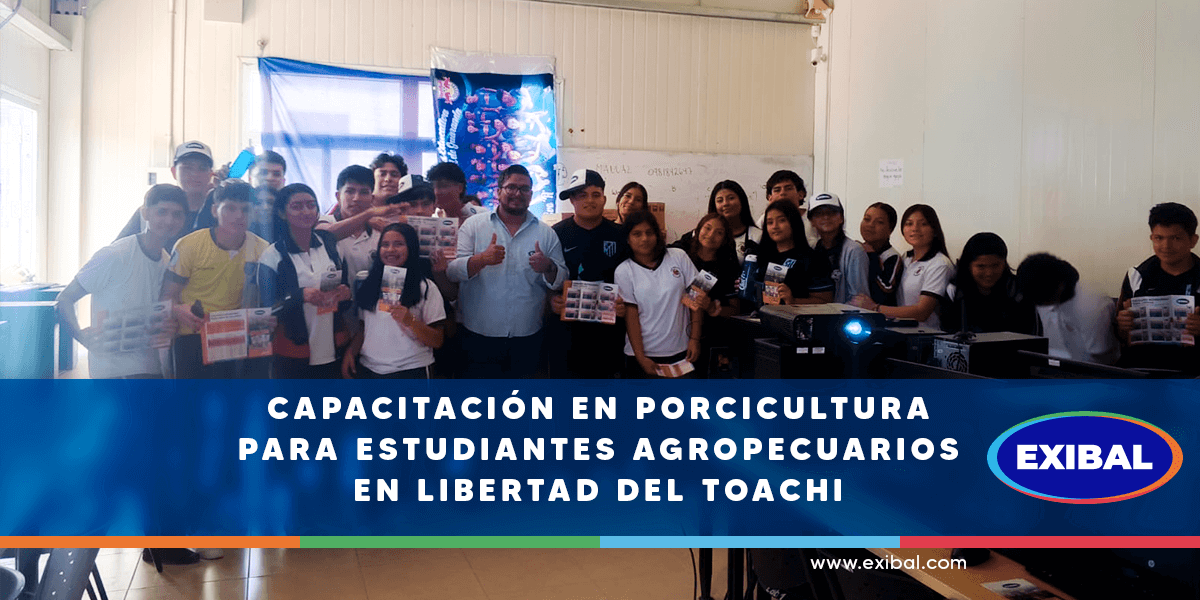 Un grupo de estudiantes agropecuarios posa junto a un instructor en un aula durante una capacitación en porcicultura organizada por EXIBAL en Libertad del Toachi. Los jóvenes sostienen folletos informativos y al fondo se observa equipo de cómputo y una pizarra.