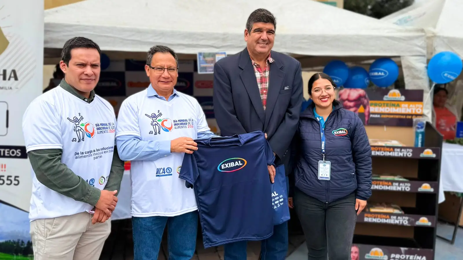 Representantes de Exibal durante evento de inocuidad alimentaria entregando camiseta institucional en feria agroindustrial