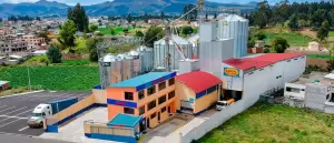 Vista aérea de la planta de procesamiento de alimentos Exibal en Chambo, Ecuador. Se aprecian edificios industriales, silos de grano y camiones de carga en el exterior.